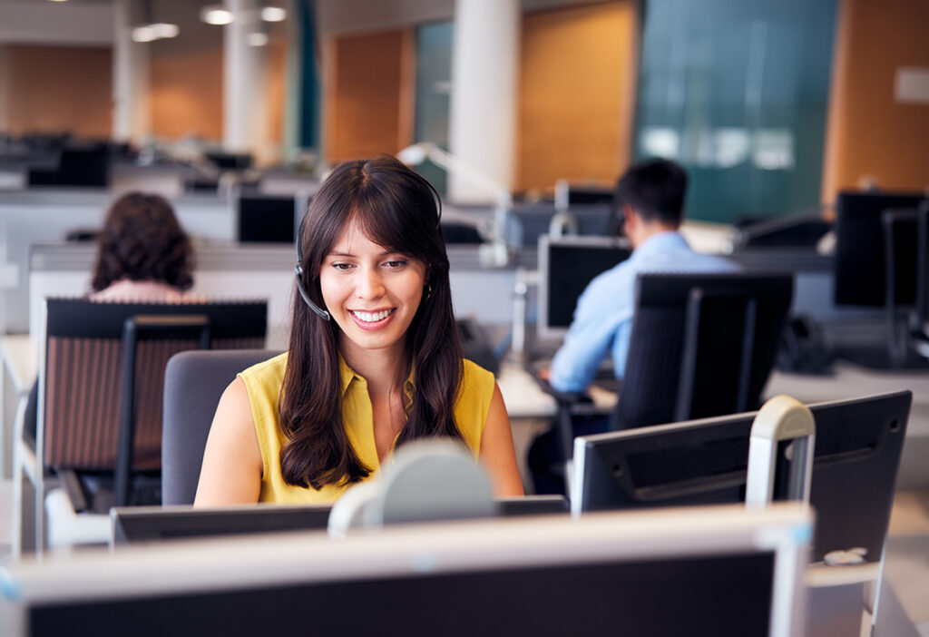 Customer service representative wearing a headset at a computer.